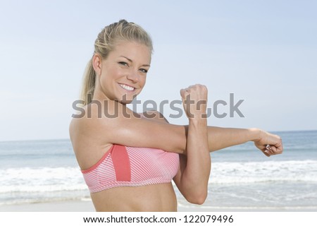 Portrait of a happy fitness woman doing arms exercise on beach