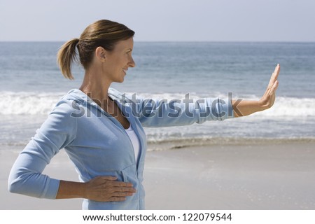 Profile view of woman in hooded top exercising on beach