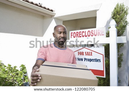 An African American sad man carrying cardboard box while moving out of the house