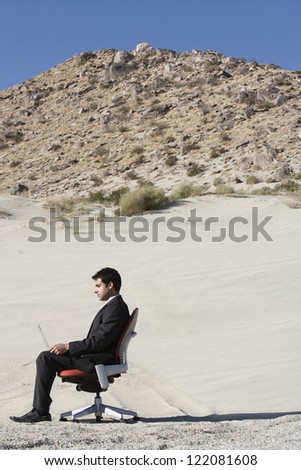 Side view of a business man working on laptop in desert