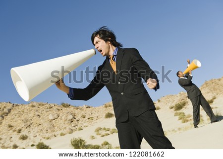 Two businessmen screaming through megaphone while standing in the desert