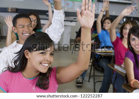 Group of happy students raising hands in classroom