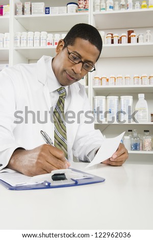 African American confident pharmacist writing prescription with medicines in the background