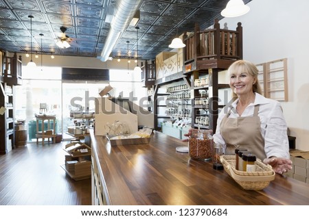 Happy senior female spice merchant standing at counter while looking away in store