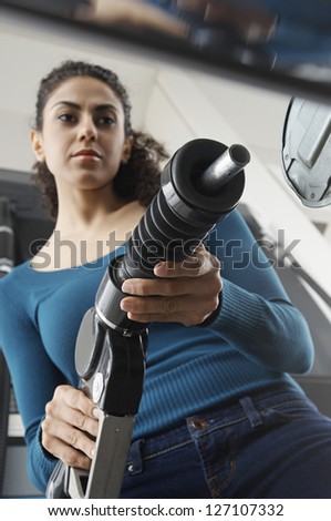 Low angle view of woman holding fuel nozzle and refueling car tank