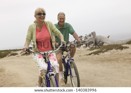 Cheerful middle aged couple riding bicycles along the beach