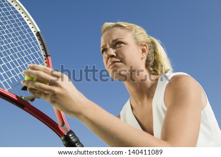Low angle view of a female tennis player preparing to serve against clear blue sky