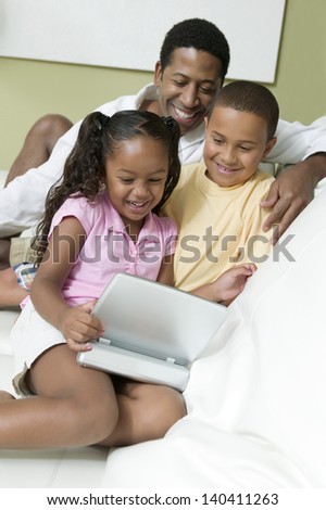 Father with son and daughter watching movie on portable DVD player in the living room