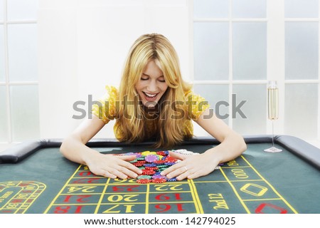Happy young blond woman at roulette table collecting chips