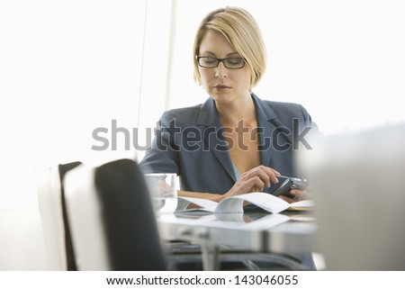 Young businesswoman with paperwork using cell phone in conference room