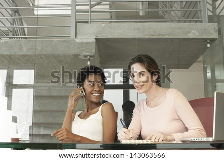 African American businesswoman using mobile phone while female colleague writing on notepad in office
