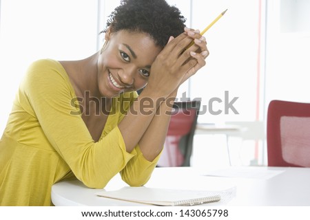 Portrait of young African American businesswoman with notepad and pencil sitting at table