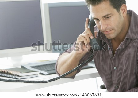 Serious businessman using landline phone at office desk