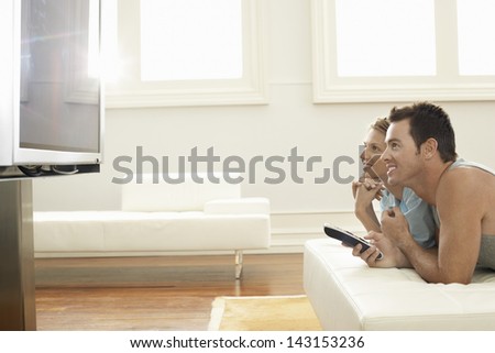 Side view of happy young couple watching plasma TV at home