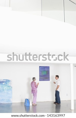Full length of mature couple discussing over painting in art gallery