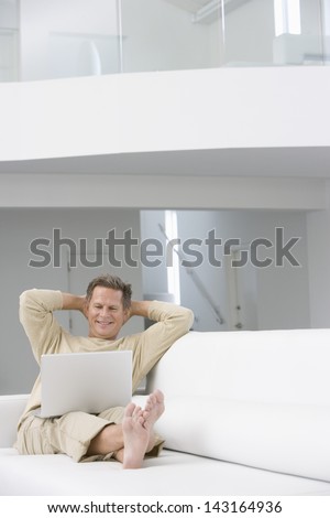 Full length of relaxed man with laptop on sofa in living room