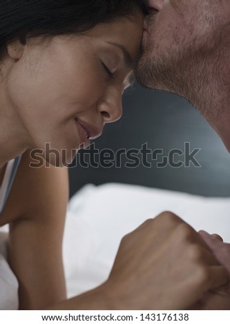 Young man kissing on woman\'s forehead in bed