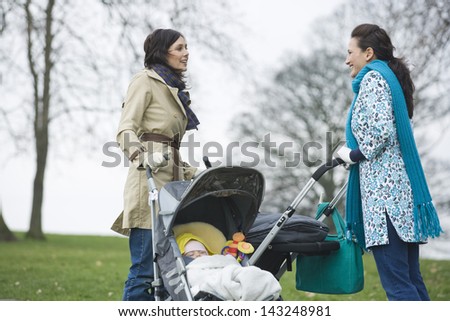 Side view of happy young mothers with strollers in park having chat