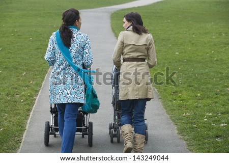 Rear view of two young mothers pushing strollers in park