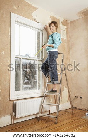 Portrait of woman holding measure tape while standing on step ladder in unrenovated house