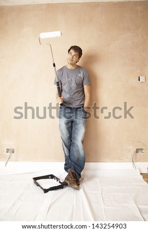 Full length of man looking at paint roller in unrenovated house