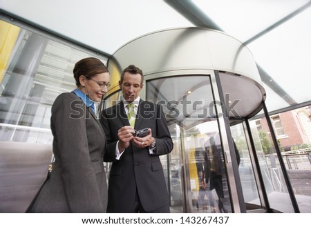 Businessman and businesswoman using PDA in front of revolving door