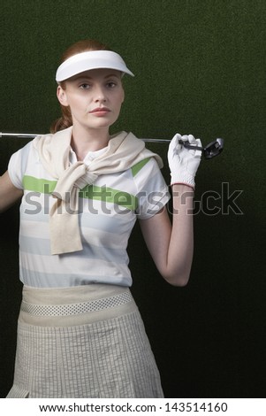 Portrait of young woman holding golf club behind shoulders against green background