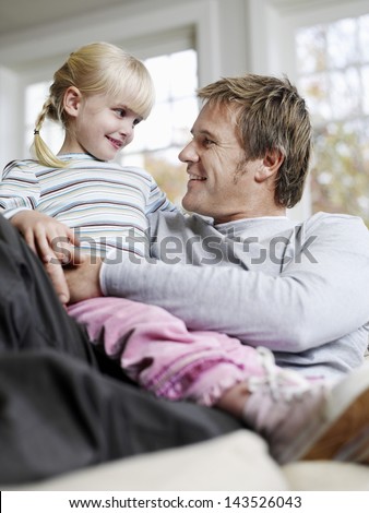 Cute little daughter sitting on father\'s lap while looking at each other at home