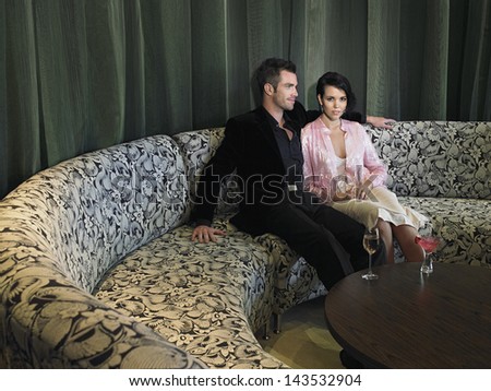 Young couple sitting on couch with drinks on coffee table in hotel lobby