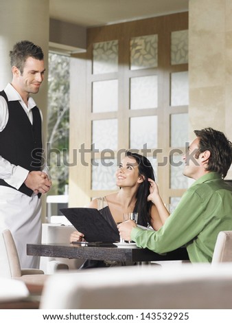 Happy young couple ordering meal to waiter at outdoor restaurant