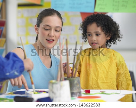 Young teacher assisting cute girl in painting during art class