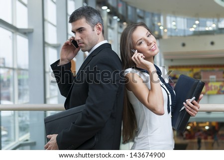 Businessman and Businesswoman back to back on mobile phones