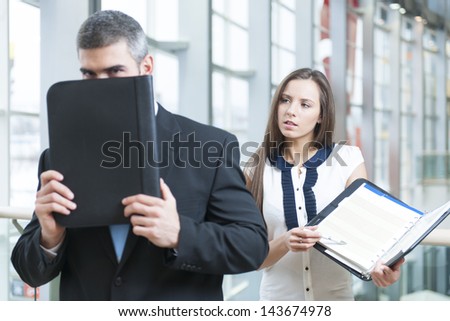 Businessman hides from coworker behind folder