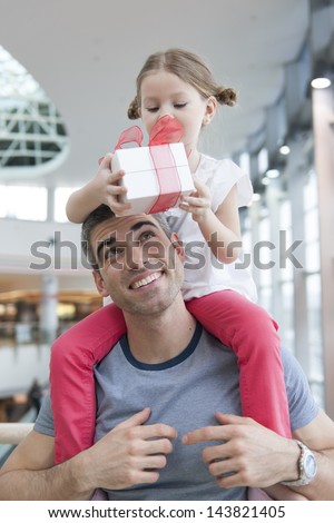 Young daughter sits on fathers shoulders and gives him a present