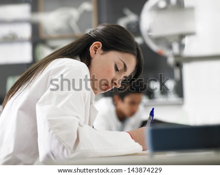 Beautiful teenage girl taking notes in science class