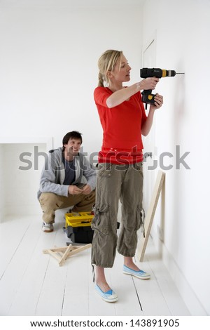 Young man watching woman drill hole in the wall at their new home