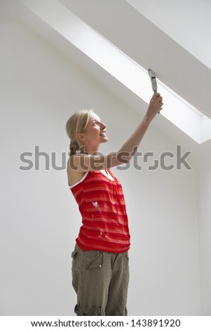 Side view of a young woman painting the ceiling slope