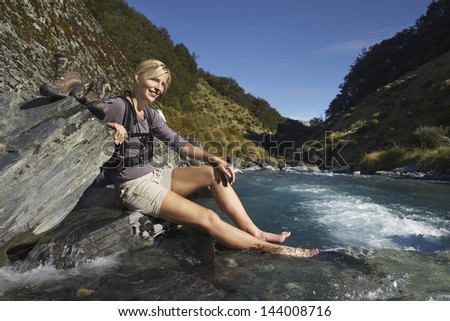 Side view of a young woman dipping her feet in forest river