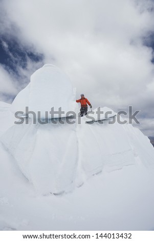 Low angle view of a male hiker standing on top of ice formation against clouds