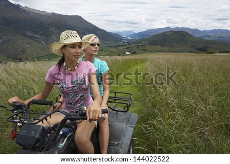Two young women riding a four wheeler through field