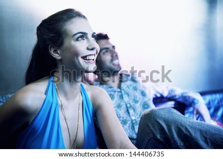 Happy young couple sitting side by side on sofa and looking up at a bar