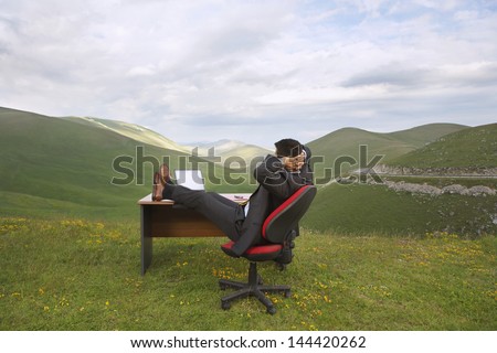 Side view of businessman relaxing with feet on desk in mountain field
