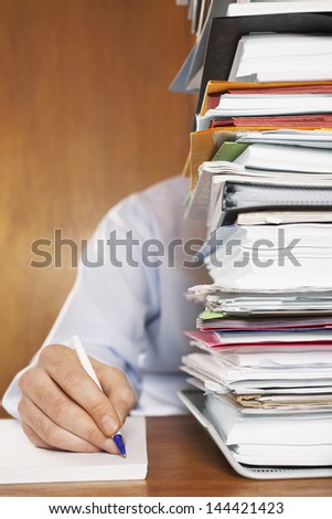 Cropped shot of a man writing document behind a stack of folders at desk