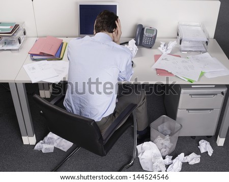 Rear view of a businessman with head in hands at office desk