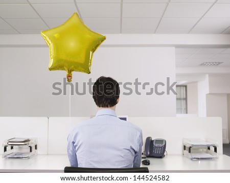Rear view of a man working alone beside balloon in office