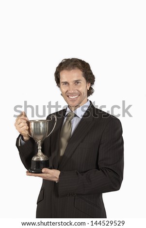 Portrait of a smiling businessman holding trophy against white background