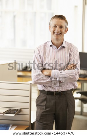 Portrait of middle aged male executive with hands folded smiling in office
