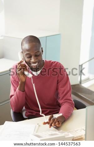Smiling African American businessman using landline at desk