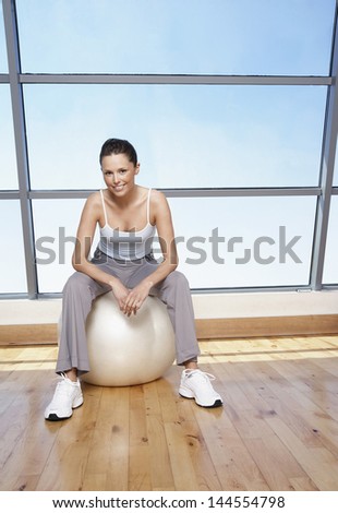 Portrait of smiling young woman sitting on exercise ball at gym
