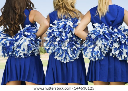 Rear view midsection of three cheerleaders holding pom poms